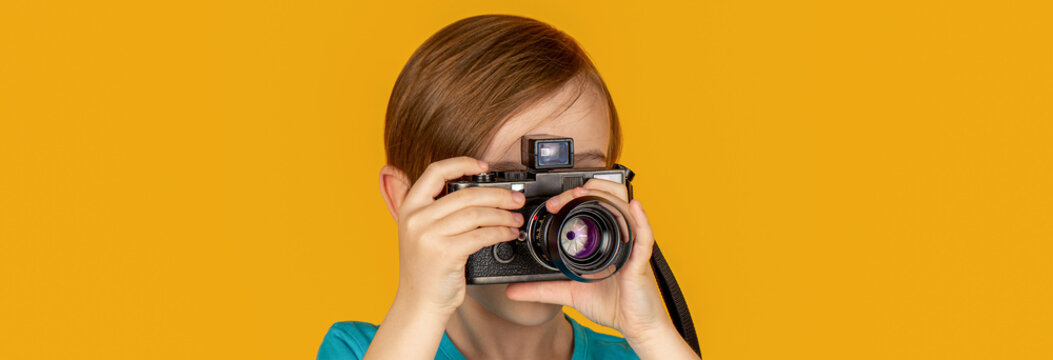 Boy using a cameras. Child looks through a vintage camera and trying the photographer profession. Studio portrait over yellow background