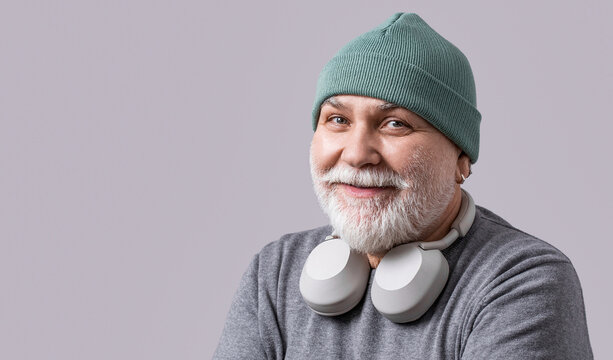 Handsome happy man in headphones listening music on gray background. Technology concept, fun. Portrait of smiling mature bearded man listening to music in headphones