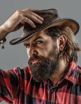 Man adjusting his cowboy hat. Man unshaven cowboys. American cowboy. Cowboy style in a plaid shirt