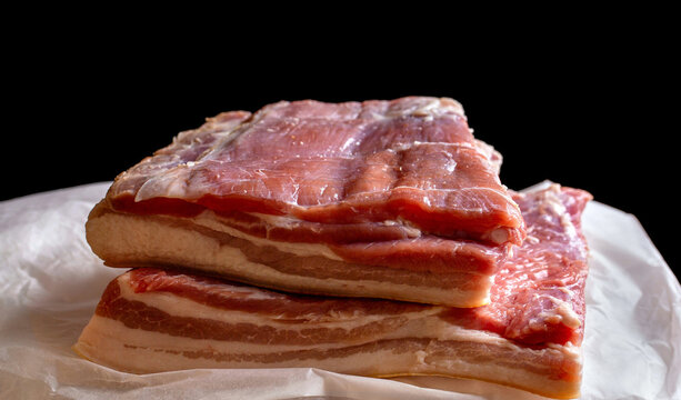 Raw meat on a wooden cutting board covered with parchment paper. Wooden board with pieces of raw pork on black background, closeup. Butcher, bacon