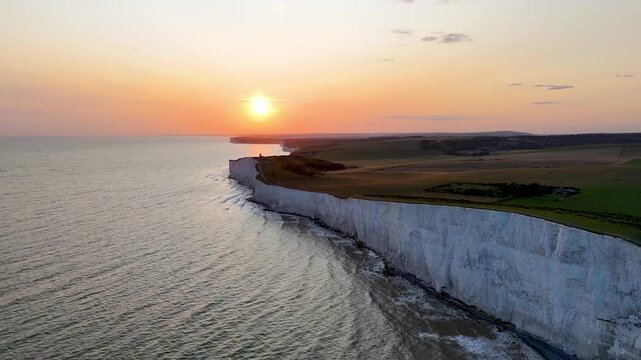 Smooth drone flight along the dramatic white chalk cliffs of Beachy Head during sunset, with golden reflections across the English Channel in East Sussex, England.