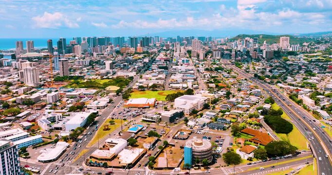 Aerial view of Honolulu urban grid and downtown skyline, Hawaii. Street network, mixed residential and commercial district, ocean and green hills in distance under partly cloudy sky.