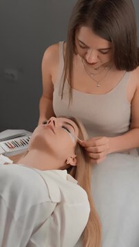 A skilled lash artist carefully attaches eyelash extensions to a client lying comfortably on a treatment bed. The beauty procedure emphasizes detail, relaxation, and expert technique