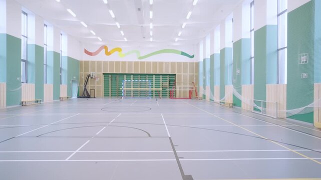 Large gymnasium shows walls basketball hoop and soccer gates on marked floor. Bright spacious hall creates active athletic atmosphere