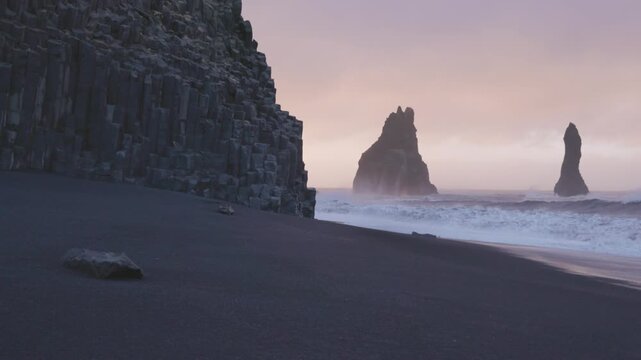 View of basalt columns and sea stacks on black sand beach at Reynisfjara in Iceland.