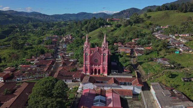 Aerial view approaches pink Gothic church in Jerico, surrounded by green hills and town