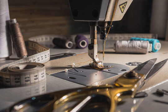 Close-up of a sewing machine with thread, measuring tape, scissors and sewing tools on a worktable. Tailoring, garment making and textile craft concept.