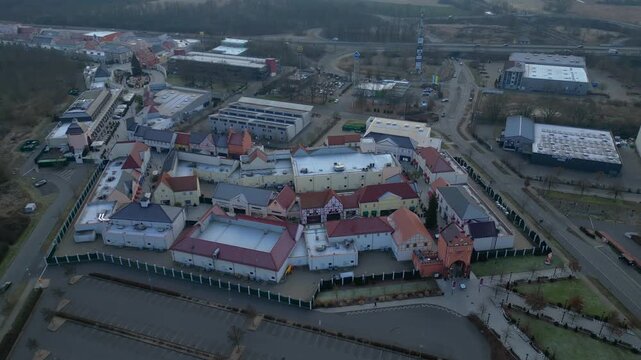 A large shopping outlet center with multiple buildings, retail stores, and an empty parking lot. Amazing aerial view drone shot panorama from above