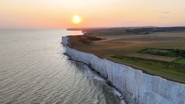 Smooth drone flight along the dramatic white chalk cliffs of Beachy Head during sunset, with golden reflections across the English Channel in East Sussex, England.