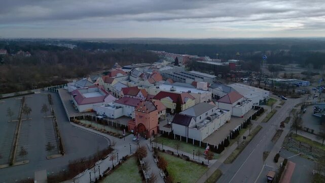 A large shopping outlet center with multiple buildings, retail stores, and an empty parking lot. Majestic aerial view drone shot panorama from above