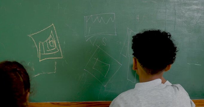 Young multicultural boy and girl student draw chart and shape on chalkboard during primary math activity, building classroom teamwork, arithmetic understanding and study confidence today at school