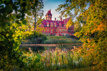 Naklejka premium Red bricks Jaunmoku castle reflected in the calm waters of old pond, Latvia, Europe. Calm summer scene of Rigas countryside, Latvia, Europe. Traveling concept background.
