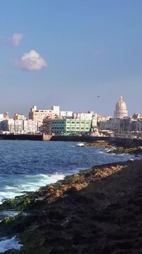 View of El Capitolio and the historic Havana coastline with crashing waves along the Malecon seawall in Havana, Havana, Cuba.
