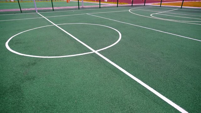 Basketball court features white markings on professional rubber surface. High metal fence surrounds athletic zone for safe team sports