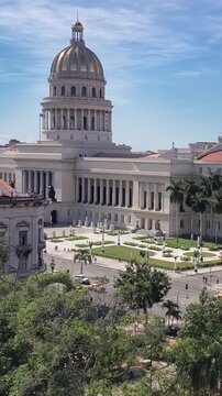 View of the neoclassical El Capitolio building with its iconic golden dome, surrounded by lush trees and urban streets in Havana, Havana, Cuba.