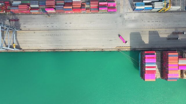 Red and blue shipping containers dock on pier extending into vibrant turquoise ocean under dark night sky, showcasing industrial logistics ideal for global trade and maritime commerce.