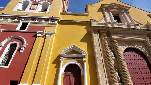 View of the historic Santisima Trinidad church in Getsemani, featuring a vibrant yellow and red facade, ornate bell tower, and colonial architecture in Cartagena, Bolivar, Colombia.
