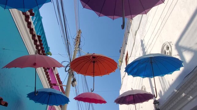 View of colorful umbrellas hanging above a narrow street in the historic Getsemani neighborhood of Cartagena, Bolivar, Colombia.