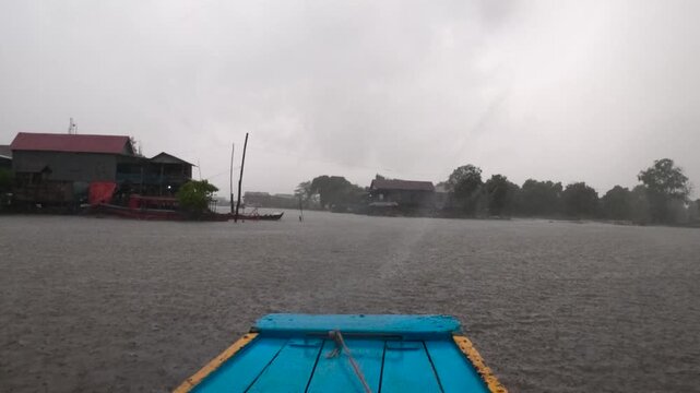 View of the floating village during a heavy rainstorm with wooden houses on stilts and boats on the water in Kampong Khleang, Siem Reap, Cambodia.