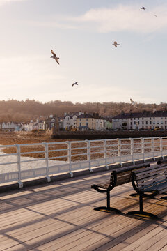 Victorian pier with benches and railings at golden hour overlooking the seafront town of Beaumaris Anglesey North Wales