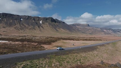 Fototapeta premium White car driving on a sandy desert road under blue sky
