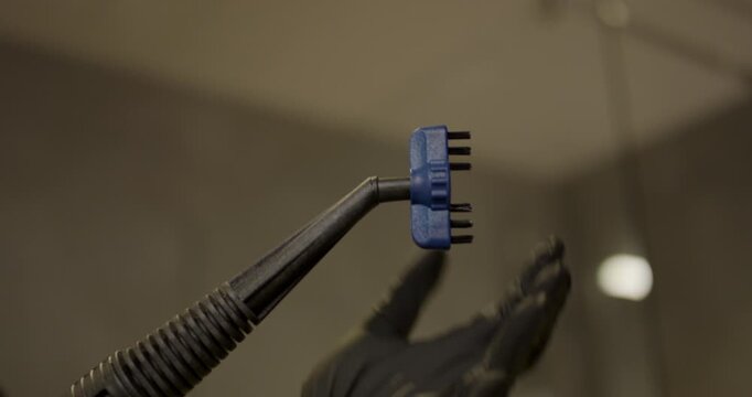 Close up view of hand in black glove attaching blue small plastic brush head onto extension steam nozzle