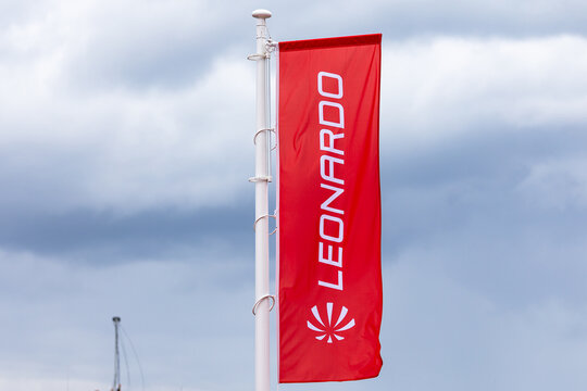 Rote Fahne mit dem Schriftzug und Logo des R&uuml;stungs- und Luftfahrtkonzerns Leonardo, aufgezogen an einem wei&szlig;en Fahnenmast vor bew&ouml;lktem Himmel.