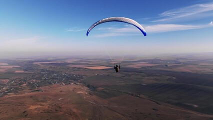 Paraglider flying over open farmland and blue sky © TamasSzora