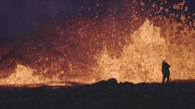 View of a person observing a powerful volcanic eruption with glowing lava fountains and dark volcanic rock in Reykjanesbaer, Iceland.