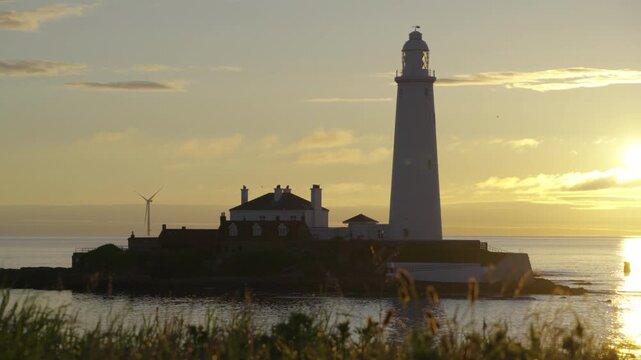Beautiful early morning shot of St Mary's Lighthouse at Whitley Bay, softly framed by backlit foreground grass during a warm summer sunrise.