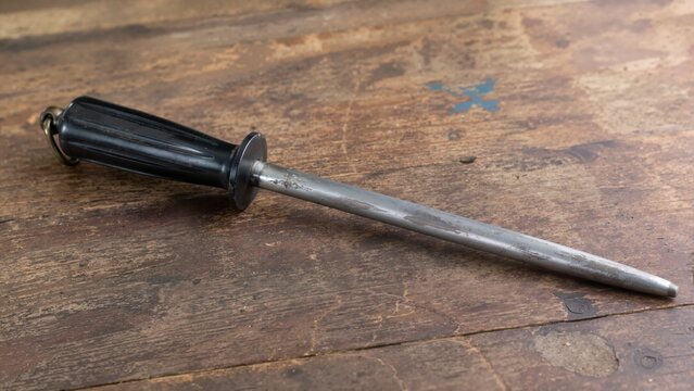 Old steel barber hone on a distressed wooden table. Vintage sharpening tool with black handle on a rustic scratched surface
