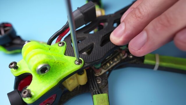 Person repairing small drone with screwdriver on blue background