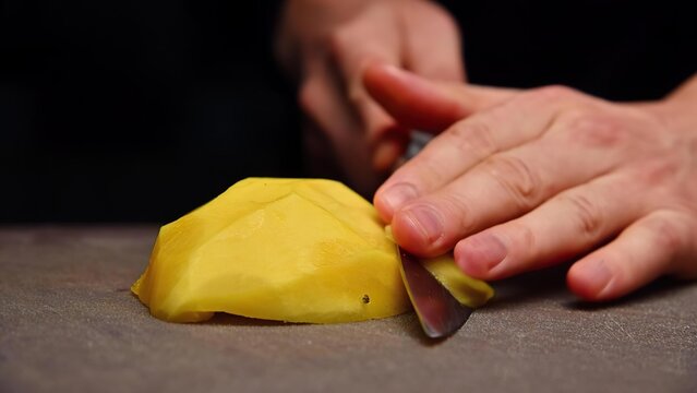 Person slicing yellow mango on a gray surface