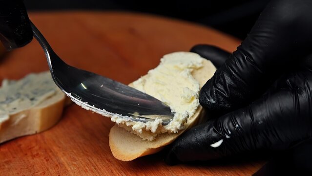 Person spreading cream cheese on bread with black gloves