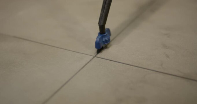 Close up view of small blue brush nozzle attachment scrubbing a dark intersection line on a floor tile