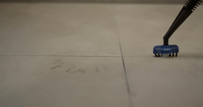 Specialized blue brush tool moving along a straight floor joint line to clean light color ceramic tile