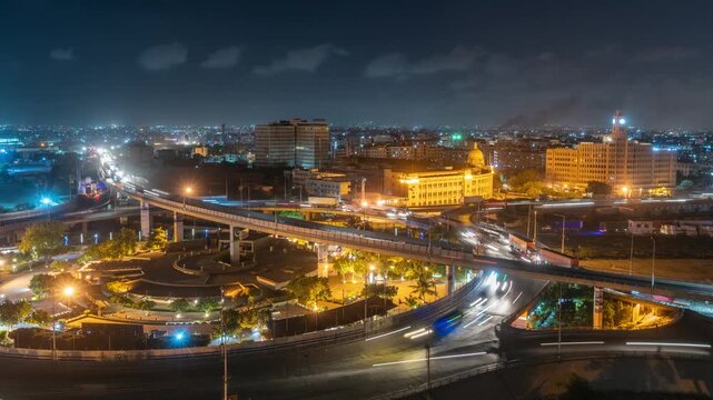 View of the illuminated Karachi Port Trust Building and surrounding highway interchange with light trails from traffic at night in Karachi, Sindh, Pakistan.