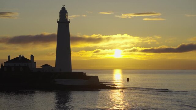Close-up shot of St Mary's Lighthouse in Whitley Bay as a brilliant golden summer sun rises directly over the North Sea horizon behind it.
