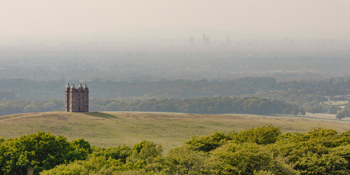 The Cage, a historic National Trust hunting tower, with the Manchester city skyline beyond on a hazy summer day