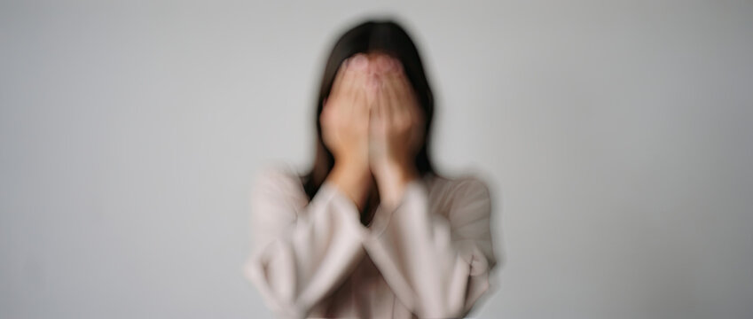 Person covering face with hands, feeling distressed, anxious, or shy, with blurred motion effect
