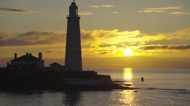 Medium shot of St Mary's Lighthouse in Whitley Bay framed against a vibrant golden sunrise over the North Sea.