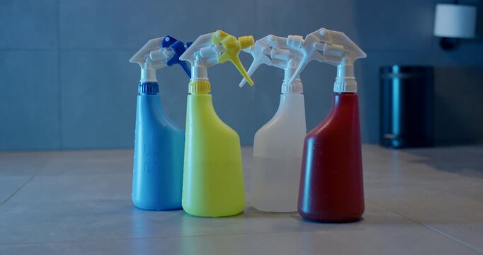 Collection of five vibrant plastic spray bottles standing grouped together on a light color tiled floor