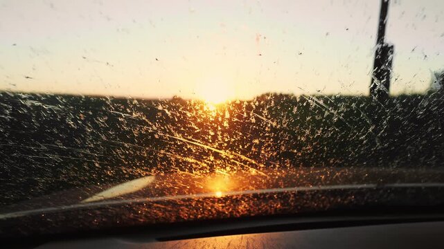 Golden sunset viewed through dusty windshield of farm machinery. Atmospheric agricultural scene showing field work conditions and rural landscape.