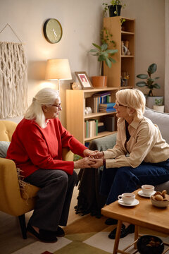 Vertical shot of senior Caucasian woman and middle aged Caucasian woman holding hands and talking at home, conveying care and support. Ideal for caregiving, counseling, family support marketing