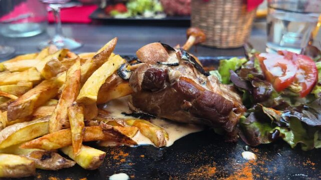 Traditional French confit de canard served with French fries and fresh green salad. Gourmet duck dish in a restaurant. High quality 4k footage