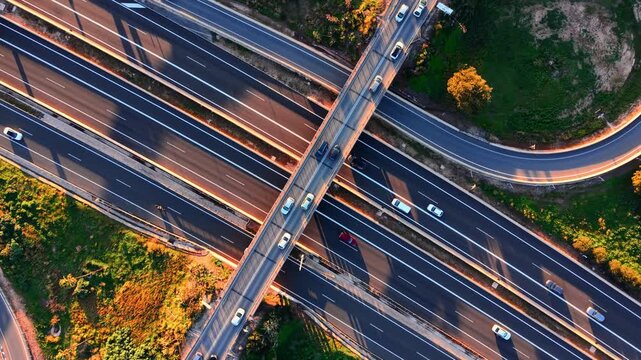 Highway intersection with crossing overpass and car, Spain. Aerial top-down view of multilane road, bridge structure, orange tree line and long shadow in warm light.