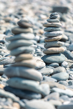 Two balanced stone stacks on beach with blurred pebble background under sunlight
