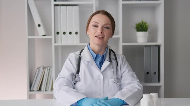 Experienced woman physician with stethoscope gestures during consultation in bright clinic workspace. Medical expert provides advice and support for health and wellness in contemporary setting