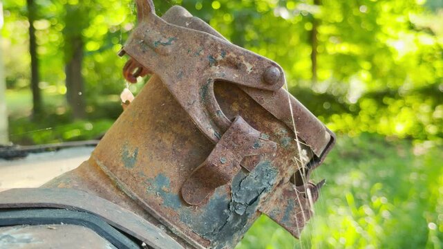 A rusty old metal latch sits abandoned in a sunny green forest. Delicate cobwebs cover the weathered object, creating a lonely mood. This quiet view brings a peaceful sense of nostalgia.