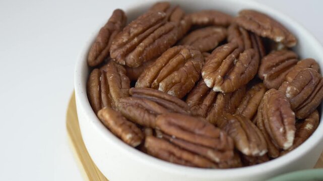 Close-up of pecan nuts in white ceramic bowl on light background. Natural organic snack rich in nutrients, healthy fats and plant protein. Clean minimalist food composition for healthy eating
